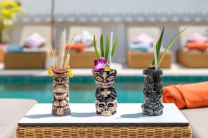 Trópusi koktélok művészi tiki bögrékben a medence mellett, vibráló és nyugodt légkört árasztva a Maya Resort Samui-ban, a Fisherman-s Village Bophutban.