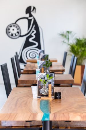 Az éttermet elegáns faasztalok és művészi asztaldíszek jellemzik, modern háttérrel, absztrakt fali dekorációval és buja zöld növényzettel.