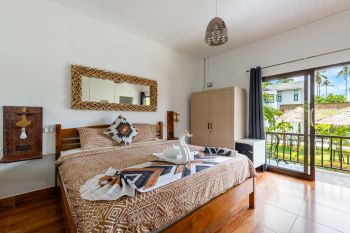 Garden Villa bedroom with a wooden double bed, woven mirror and glass doors opening onto the balcony.