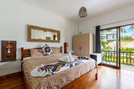 Garden Villa bedroom with a wooden double bed, woven mirror and glass doors opening onto the balcony.