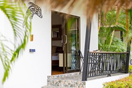 Entrance to a Garden Villa with Mayan wall art, glass door and a terrace framed by palms.